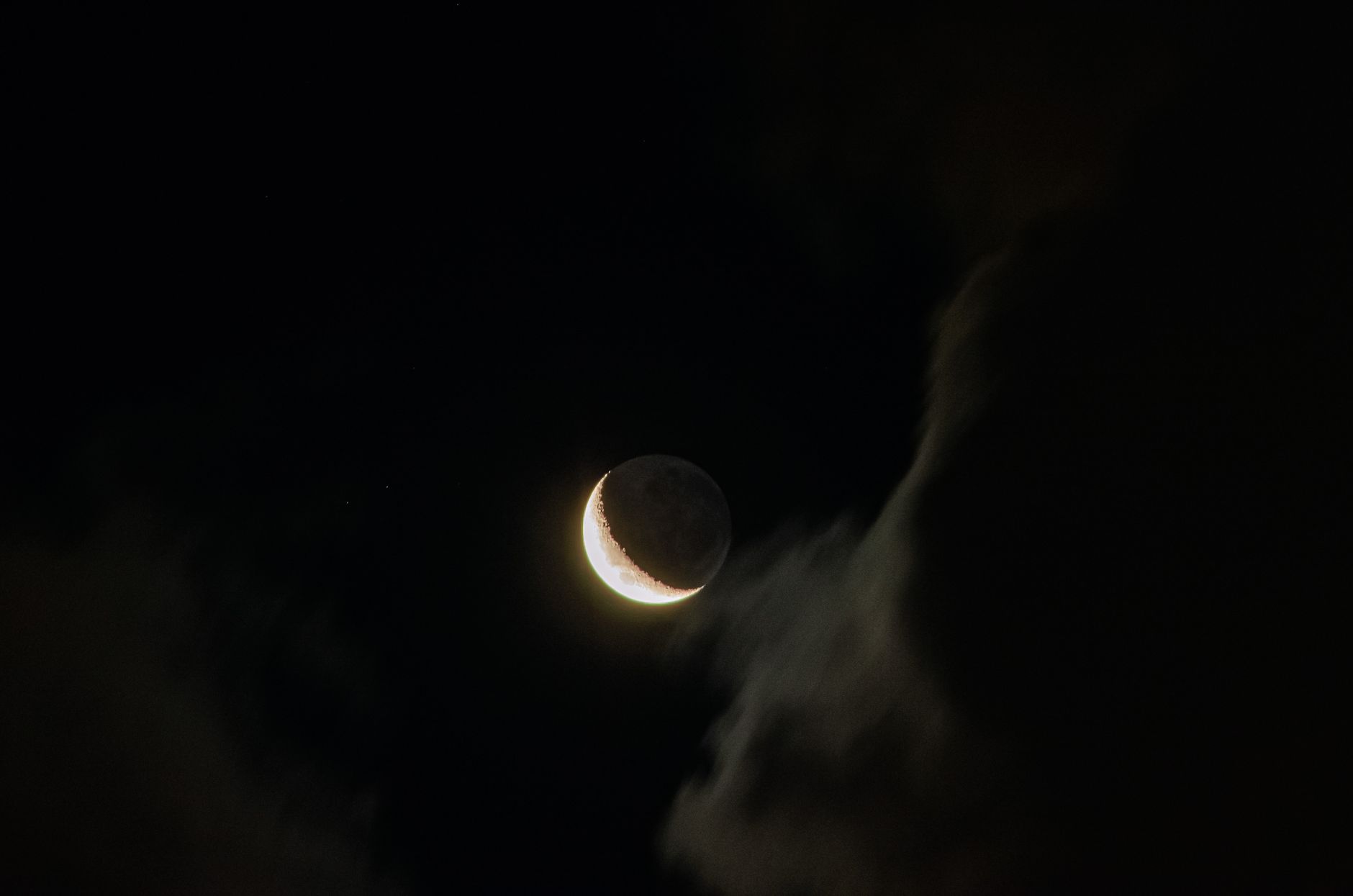 A striking crescent moon shines bright amidst dark, dramatic clouds in the night sky.